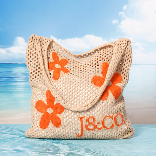 Beige woven bag with orange flowers and 'J&CO' branding on a beach setting